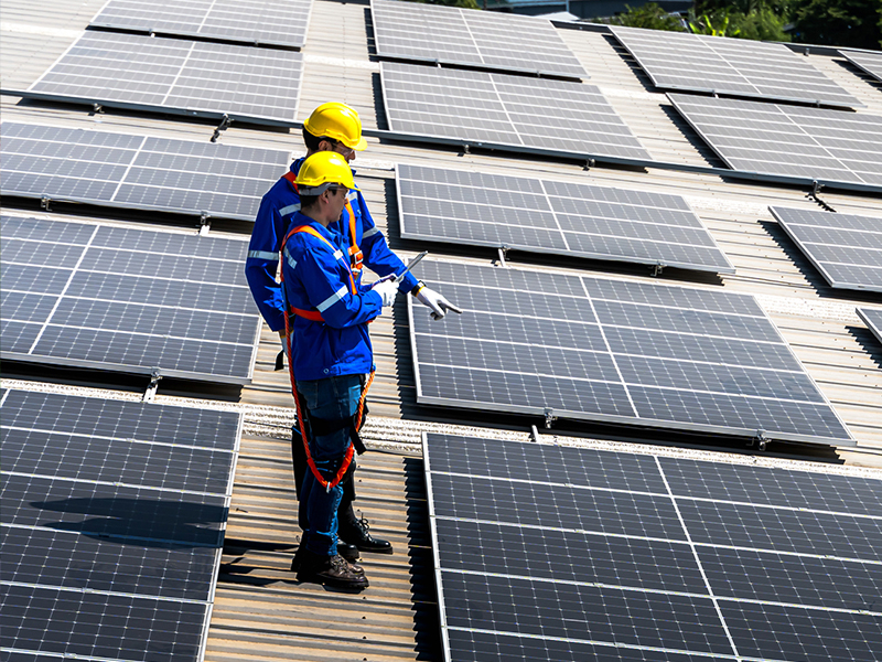 two people with blue suits on, harnesses and yellow hats working on a roof with solar panels