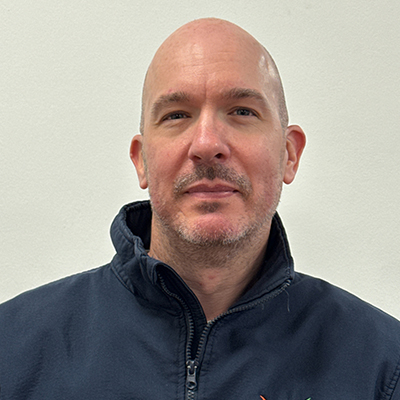 Person with no hair and a moustache wearing a blue zip up jacket