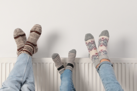 three people sat on the floor with their legs on top of a radiator.