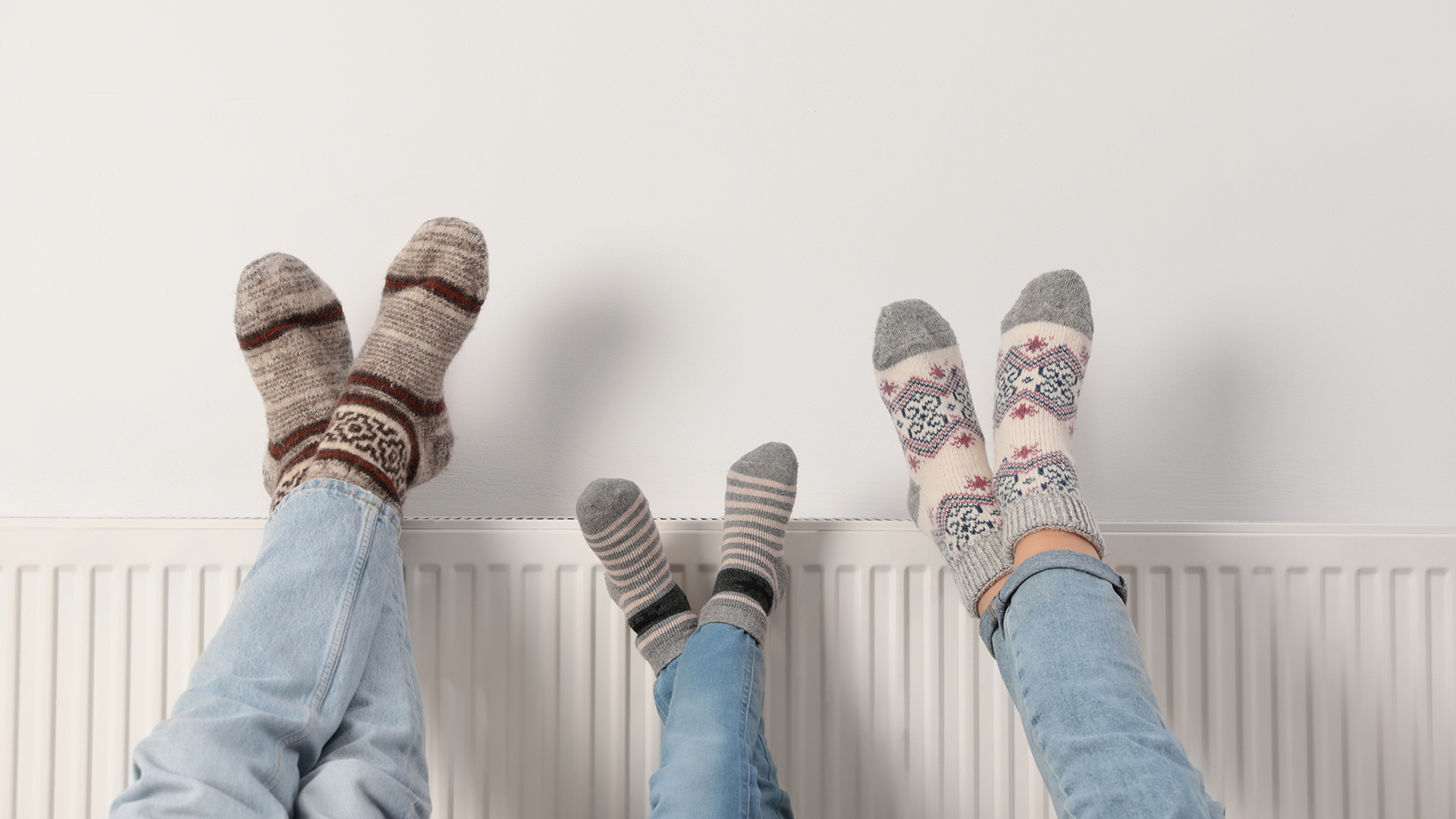 three people sat on the floor with their legs on top of a radiator.